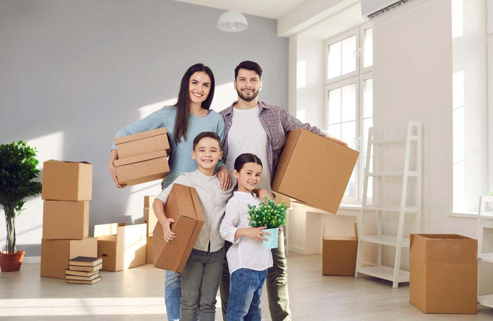 father, mother, daughter and son smiling holding boxes in a new house