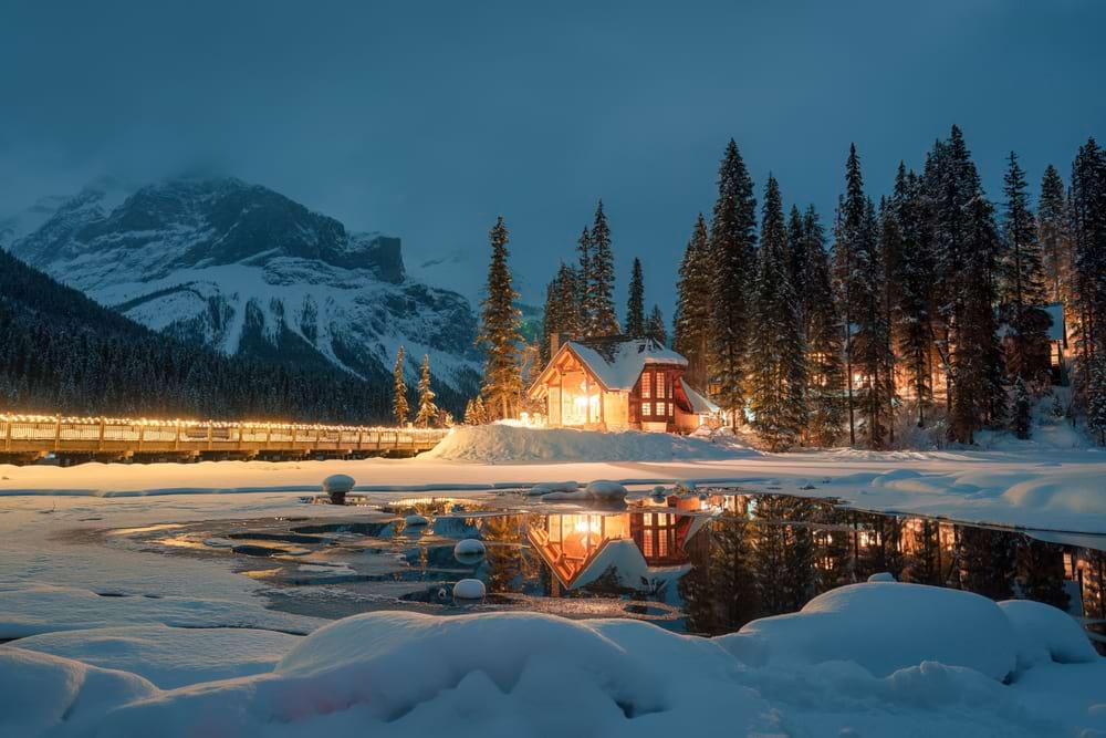 cottage in snow by lake and mountain at night